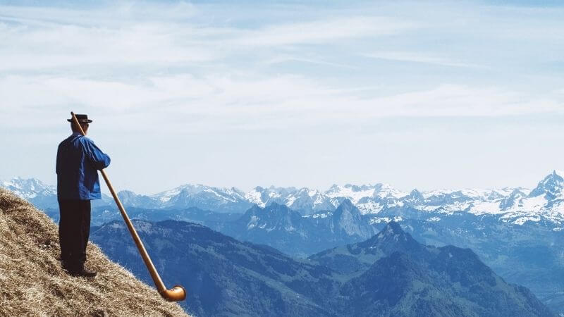 アルプス山脈を見渡せる草原でアルプホルンを演奏する男性