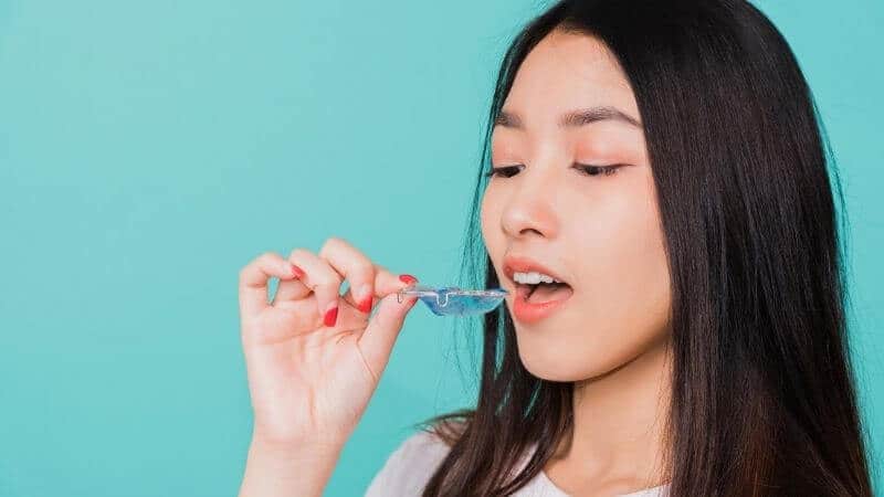 日本における歯列矯正の現実。歯の矯正器具を手にする日本人女性